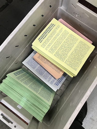 Cette image montre une caisse en plastique La Poste dans laquelle sont entreposés des tas du premier tract de la collection Positions d’éditeurices : _Vers un modèle rentable pour une maison d’édition autonome_ (Marc Fischer